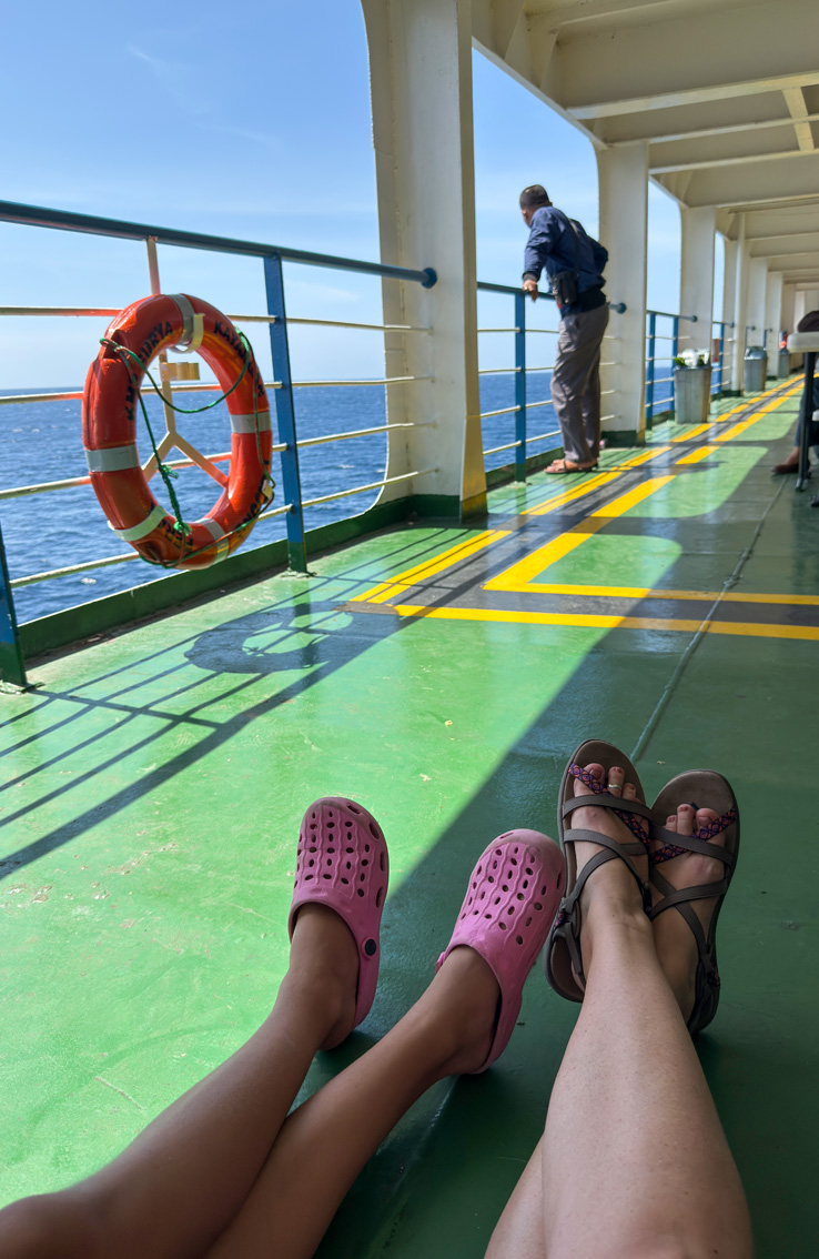 Come arrivare a Sumbawa Ovest. Vista di due gambe allungate sul pavimento del traghetto, una di una donna adulta e una di una bambina.