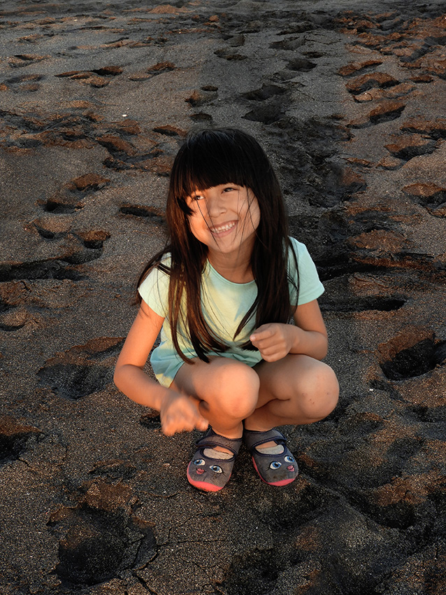 Canggu, Lara siede sulla spiaggia nera di Seseh. 